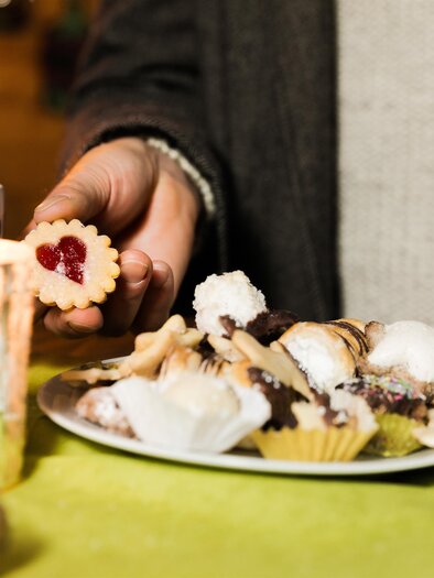 A plate with various candies and cookies is held by a hand. In the background, two cups and a candle are on a table. | © Lupi Spuma