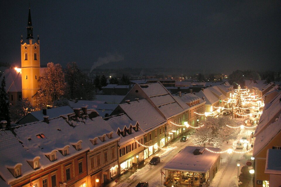 Eine malerische Stadt bei Nacht, bedeckt mit Schnee und festlicher Beleuchtung. Im Hintergrund steht ein hoher Turm und die Straße ist voller Lichter. | © FantaFilm