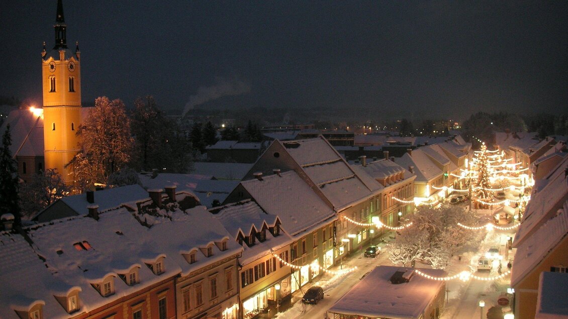 Eine malerische Stadt bei Nacht, bedeckt mit Schnee und festlicher Beleuchtung. Im Hintergrund steht ein hoher Turm und die Straße ist voller Lichter. | © FantaFilm