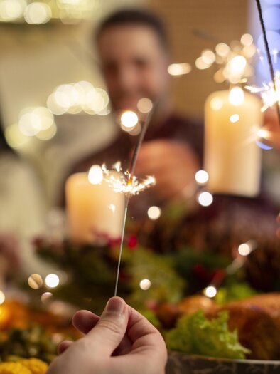 A festive celebration with sparkling sparklers and delicious food on the table. In the background, happy people can be seen enjoying the atmosphere. | © MALU