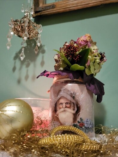 Ein dekoriertes Glas mit einem Bild von einem alten Mann und bunten Blumen. Daneben liegen goldene Dekorationen und eine glitzernde Kugel. | © Malermeisterbetrieb Enzi