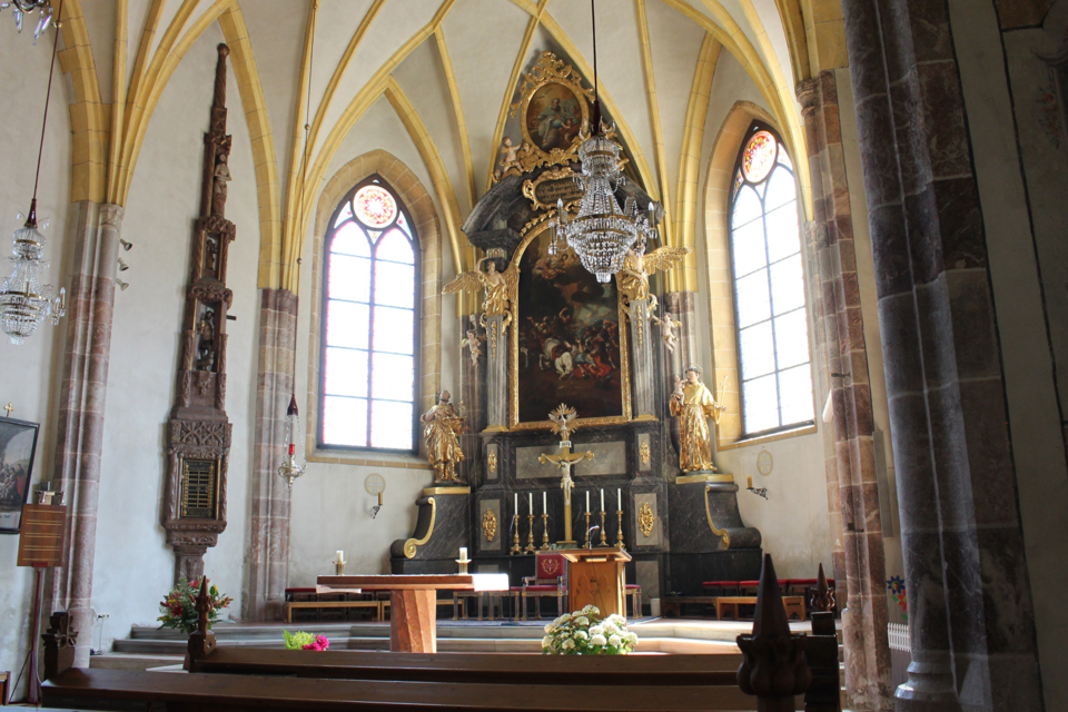 Eine helle Kirche mit hohen Gewölben und bunten Fenstern. Der Altarbereich ist kunstvoll gestaltet und gut beleuchtet.