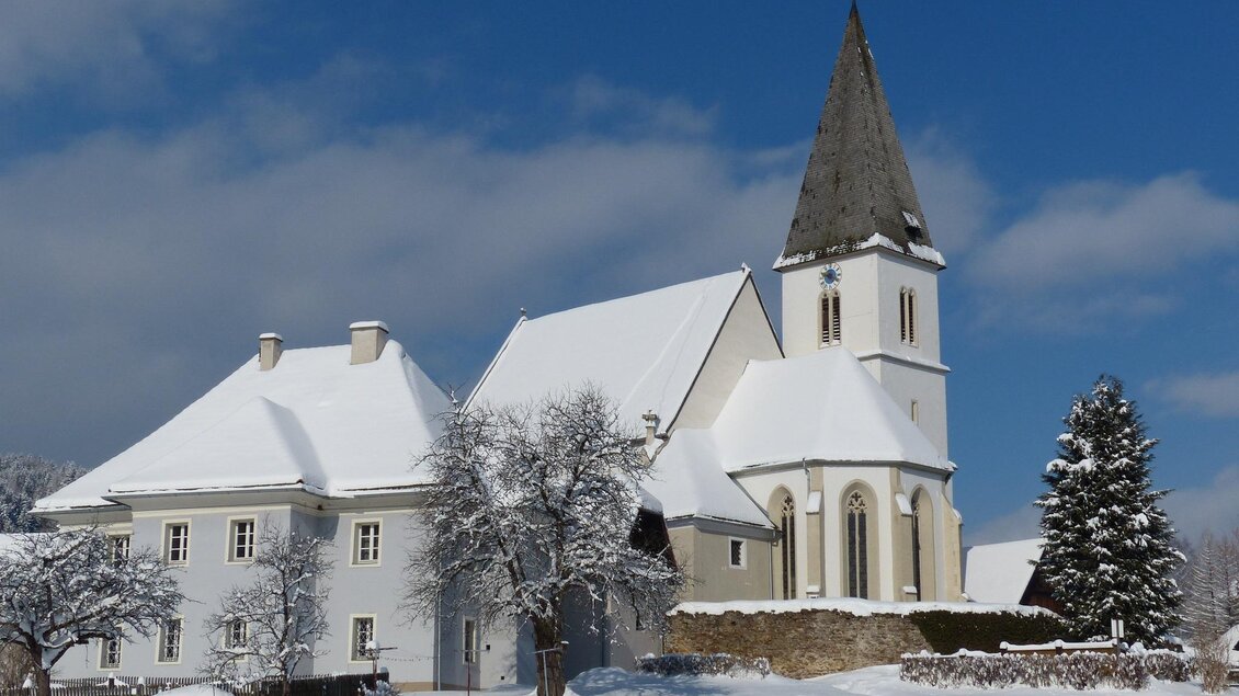 Eine verschneite Landschaft mit einem hübschen Gebäude und einer Kirche. Der Himmel ist klar und blau. | © Gemeinde Hirschegg-Kopp Josef