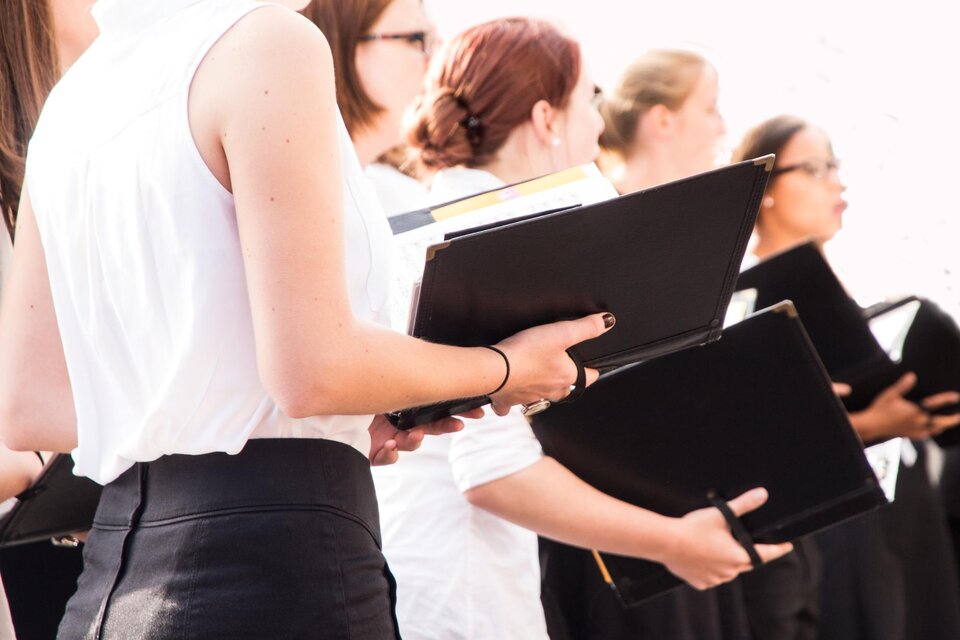 Eine Gruppe von Sängern steht in Schwarzem und Weiß, während sie Notenblätter in der Hand halten. Die Atmosphäre ist konzentriert und musikalisch. | © TV Südsteiermark - Adobe Stock