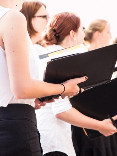 A group of singers stands in black and white, holding sheet music in their hands. The atmosphere is focused and musical. | © TV Südsteiermark - Adobe Stock