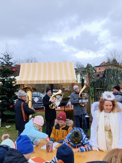 A Christmas market with festively dressed people and a music ensemble. In the foreground, children are playing, and there are Christmas-decorated stalls. | © Ortverschönerungsverein Jamm