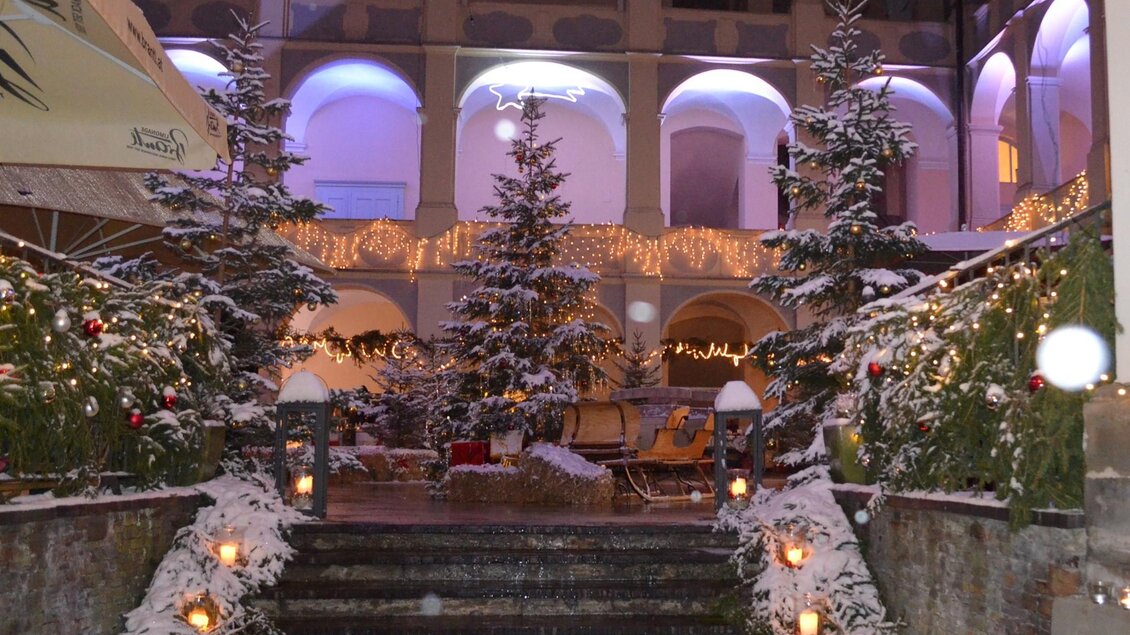 Ein winterlicher Innenhof mit schneebedeckten Tannenbäumen und festlicher Beleuchtung. Gemütliche Sitzgelegenheiten laden zum Verweilen ein. | © Lipizzanergestüt Piber SRS GöR