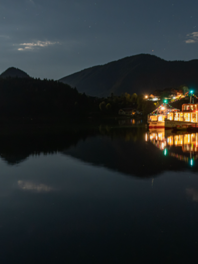 A tranquil lake at night, surrounded by mountains and gentle clouds. The light of the moon reflects on the surface of the water. | © Schiffsfahrt Grundlsee