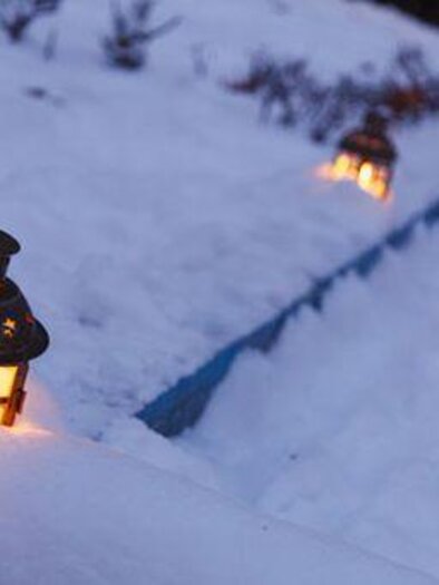 A beautiful winter landscape with snow and several lanterns. The lanterns glow warmly in the cold environment. | © TVB Thermen- & Vulkanland
