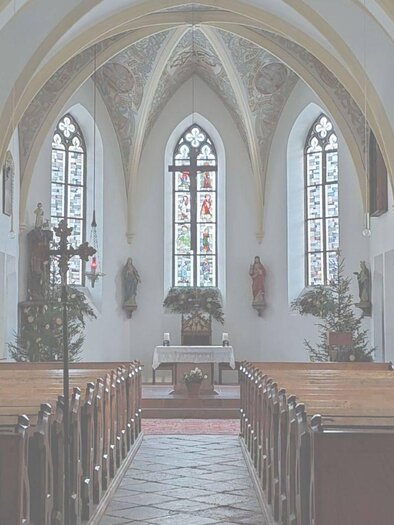 A quiet church with wooden pews and colorful windows. In the background, there is an altar with decorations. | © Monika Baumgartner