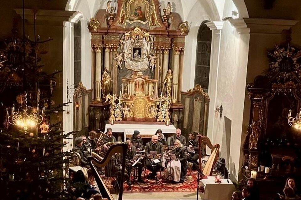 Eine festliche Kirchenaufführung mit Musikern, die in einer schön dekorierten Kirche spielen. Der Altar ist prächtig geschmückt und es gibt Weihnachtslichter im Raum. | © TMK Pichl