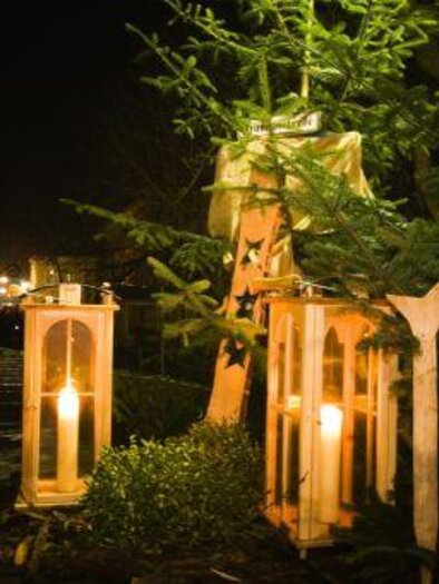 Lampen in Laternen leuchten in der Dunkelheit neben einem Weihnachtsbaum. Im Hintergrund sind festliche Lichter sichtbar. | © TVB Thermen- 6 Vulkanland