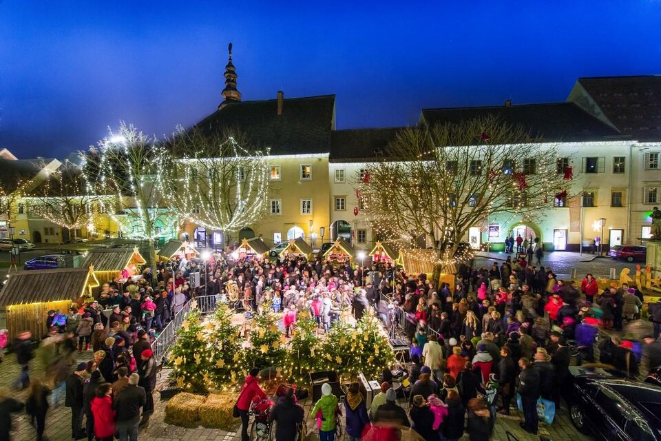 Ein belebter Weihnachtsmarkt mit vielen Menschen und festlicher Beleuchtung. Umgeben von traditionellen Ständen und geschmückten Bäumen strahlt die Atmosphäre Gemütlichkeit aus. | © TV Thermen- & Vulkanland