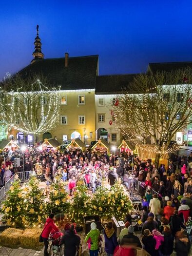 A bustling Christmas market with many people and festive lighting. Surrounded by traditional stalls and decorated trees, the atmosphere radiates coziness. | © TV Thermen- & Vulkanland