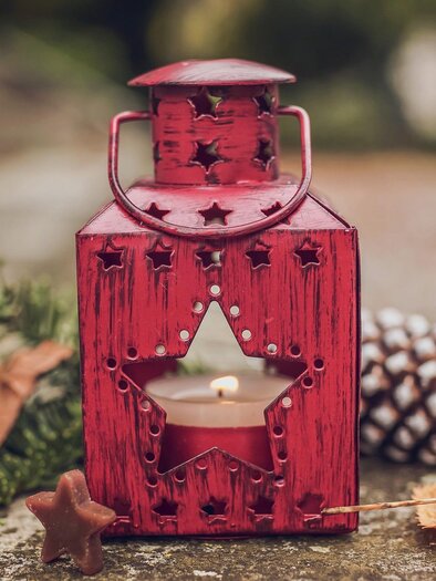 A red lantern with a star and a candle stands on the ground. Around it are leaves, stars, and a pine cone. | © pixabay