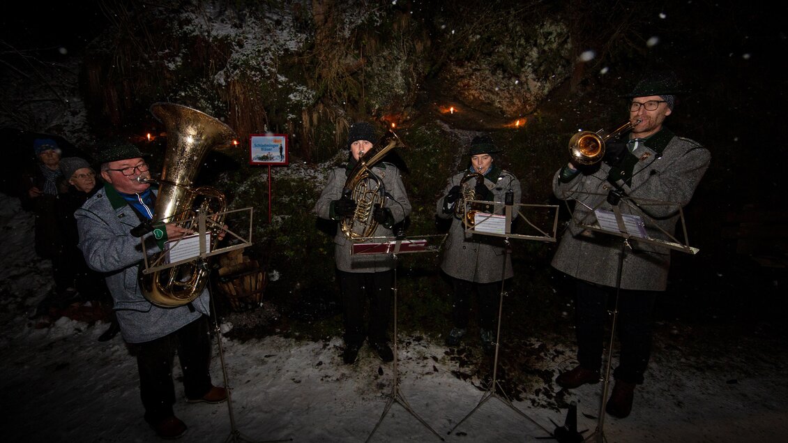 Eine Bläsergruppe spielt Musik in einer schneebedeckten Umgebung. Im Hintergrund sind schwaches Licht und eine fröhliche Atmosphäre zu sehen. | © Herbert Raffalt