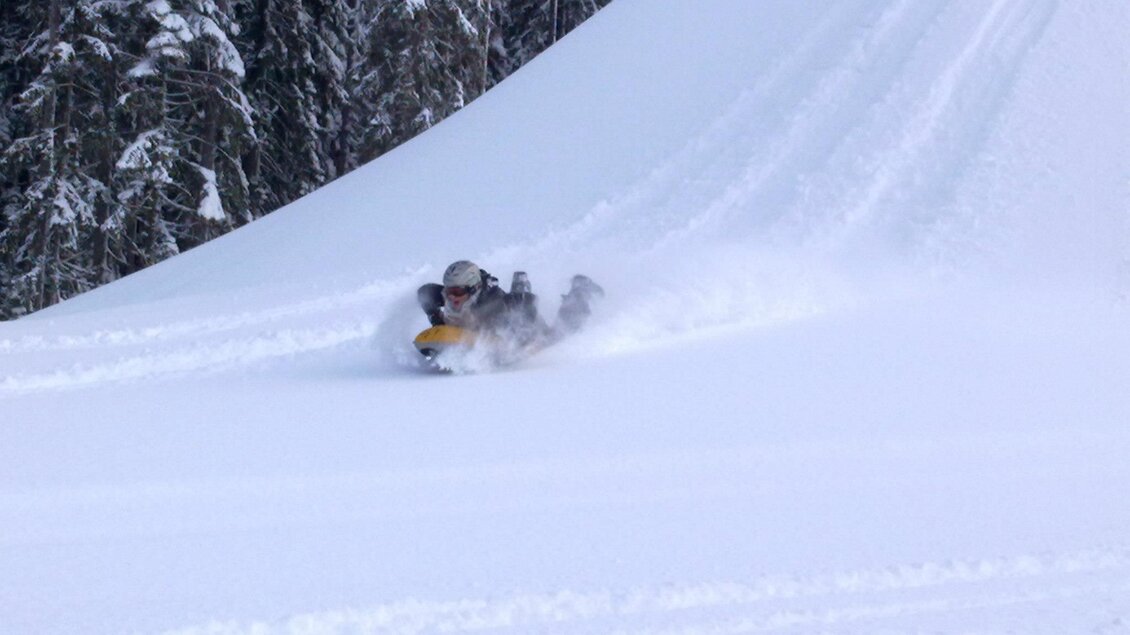 Ein Mensch fährt mit einem Schlitten einen verschneiten Hang hinunter. Umgeben von verschneiten Bäumen genießt er den Winterspaß. | © OCT