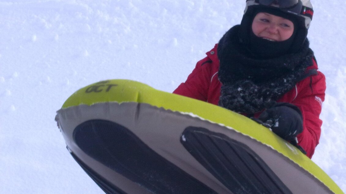 Ein Kind steht im Schnee mit einem gelben Schlitten. Es trägt eine rote Jacke und einen Helm. | © OCT