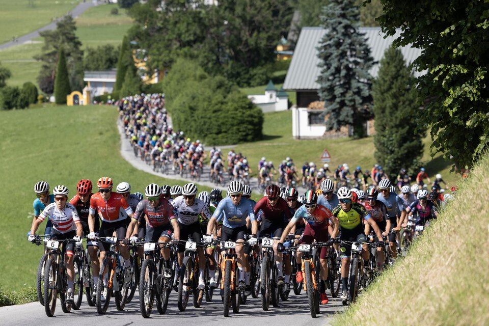 Großes Fahrerfeld von Mountainbikern beim Start der Alpentour, die Straße hinauf durch grüne Landschaft. | © Marketa Navratilove