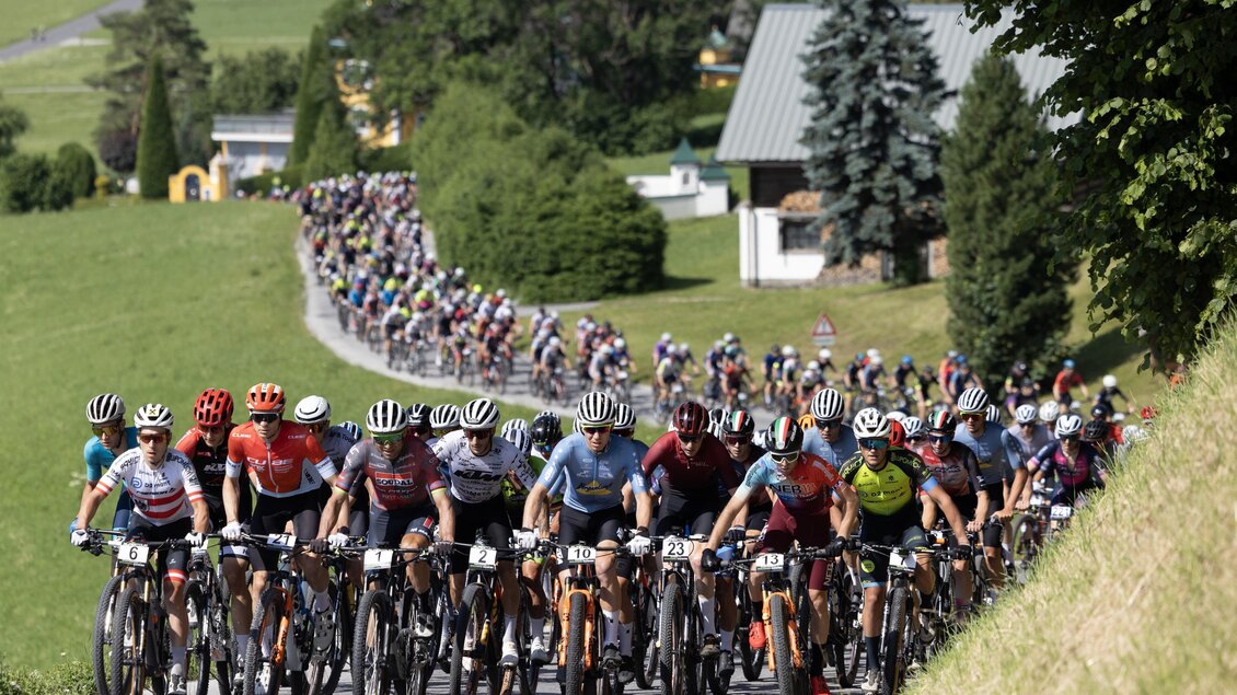 Großes Fahrerfeld von Mountainbikern beim Start der Alpentour, die Straße hinauf durch grüne Landschaft. | © Marketa Navratilove