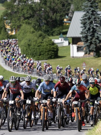 Großes Fahrerfeld von Mountainbikern beim Start der Alpentour, die Straße hinauf durch grüne Landschaft. | © Marketa Navratilove