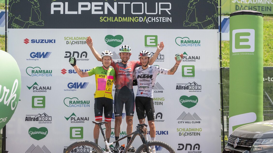 Drei Mountainbiker stehen jubelnd auf dem Siegerpodest der Alpentour Schladming-Dachstein. | © Regina Stanger