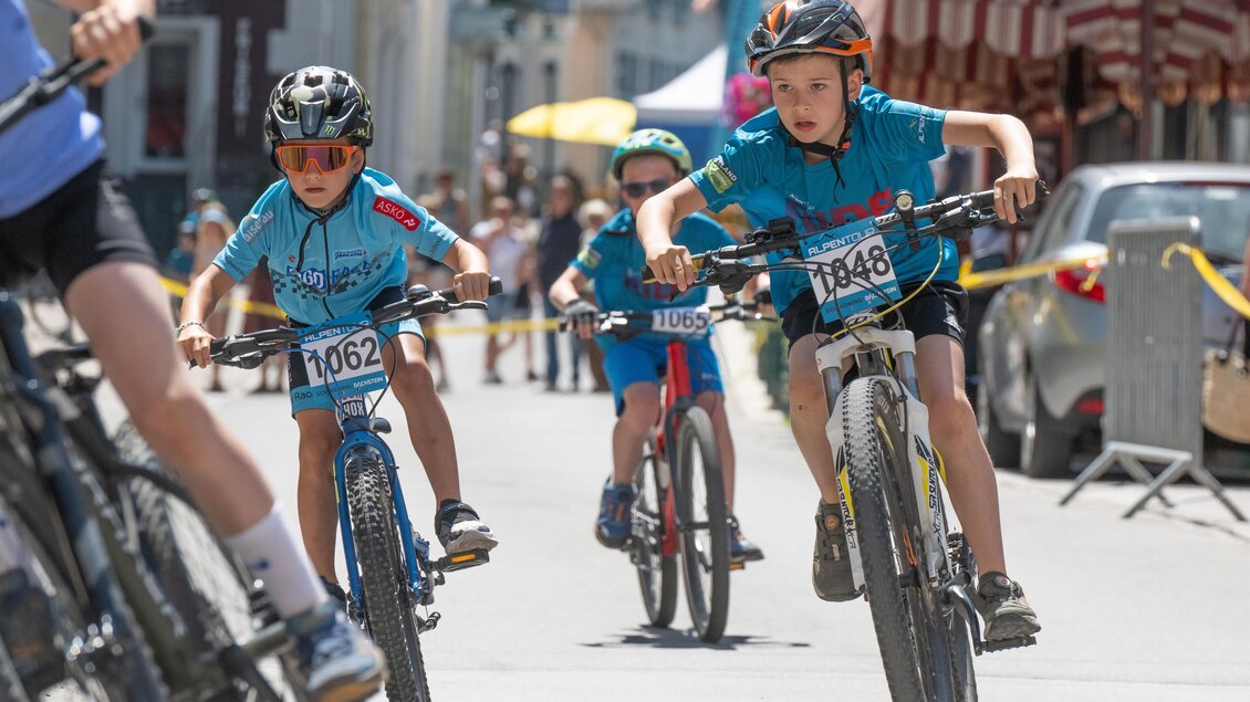 „Kinder nehmen konzentriert an einem Radrennen in der Stadt teil, fahren mit blauen Trikots und Helmen. | © Regina Stanger
