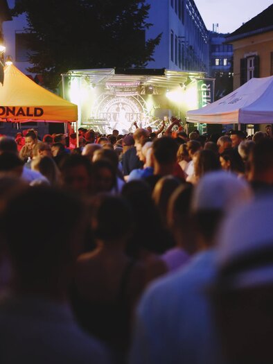 A lively event at dusk with many people. There are several stalls, including one with the sign "FC-DONALD". | © Tauser