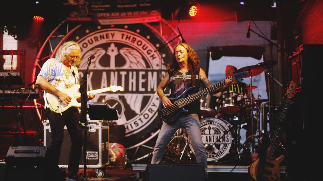 Eine Band spielt live auf der Bühne. Der Gitarrist und der Bassist sind im Vordergrund zu sehen, umgeben von Musikinstrumenten. | © Tauser