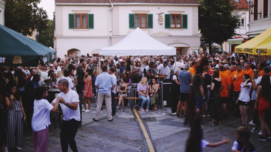 Eine lebhafte Menge feiert auf einem Platz mit zahlreichen Menschen und Ständen. Einige tanzen, während andere sich unterhalten und die Atmosphäre genießen. | © Tauser