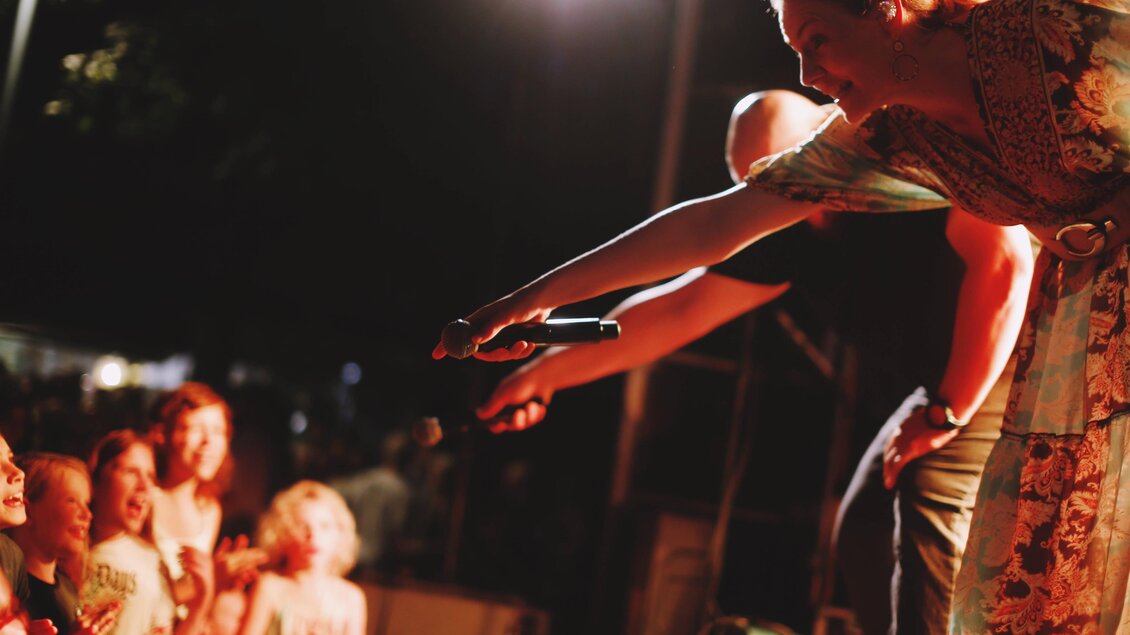 Eine Künstlerin reicht ein Mikrofon an das Publikum. Kinder schauen begeistert zu und applaudieren. | © Tauser