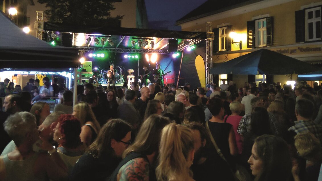 Eine große Menschenmenge versammelt sich vor einer Bühne mit bunten Lichtern. Es ist Abend und die Stimmung ist festlich. | © Nina Darnhofer