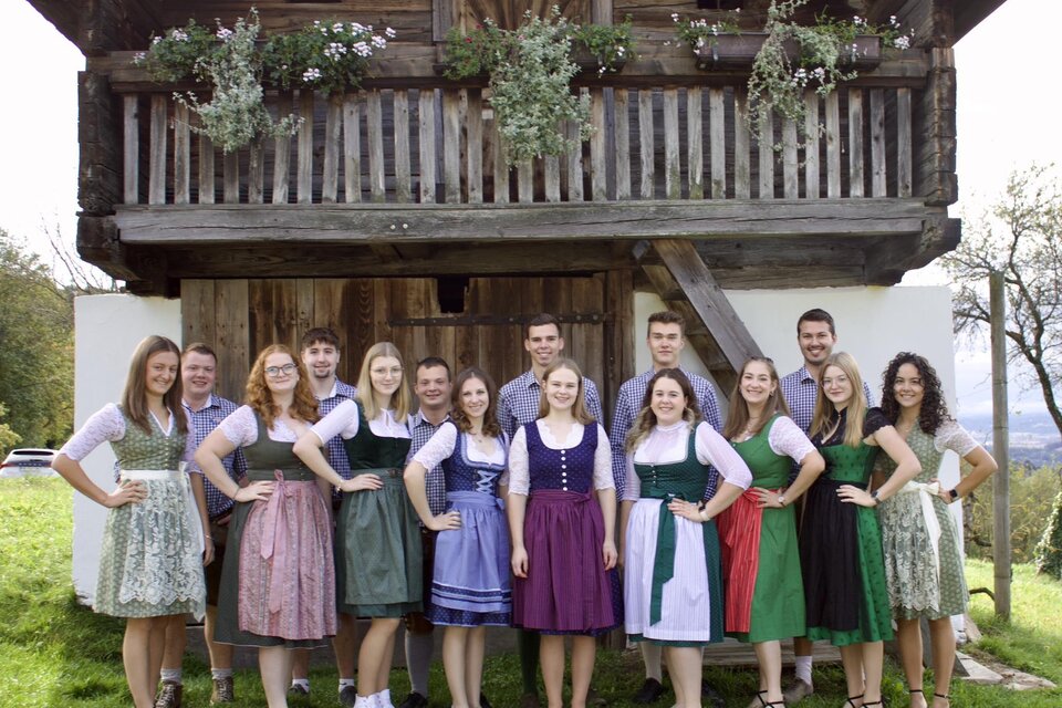 Eine Gruppe von Personen in traditioneller Tracht steht vor einem rustikalen Fachwerkhaus. Die Männer und Frauen lächeln und posieren gemeinsam in einer schönen ländlichen Umgebung. | © Landjugend Stubenberg