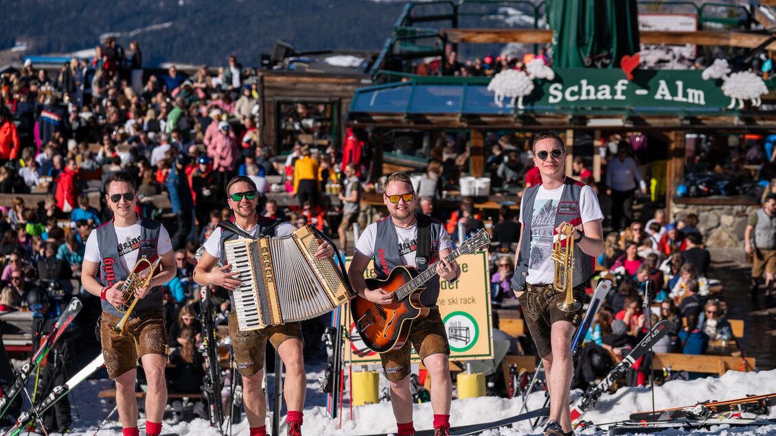 Eine lebhafte Winterparty auf den Skipisten mit einer Band, die traditionelle Musik spielt. Viele Menschen sind im Hintergrund versammelt und genießen die Atmosphäre. | © Mario Egger