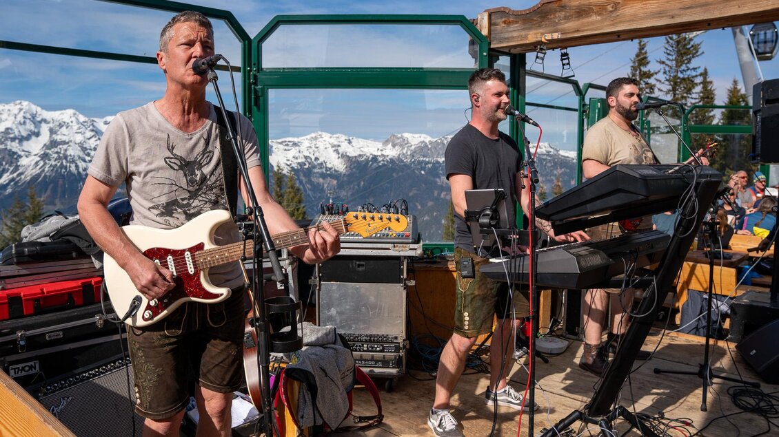 Eine Band spielt live in den Bergen. Im Hintergrund sind die schneebedeckten Gipfel und ein blauer Himmel zu sehen. | © Mario Egger