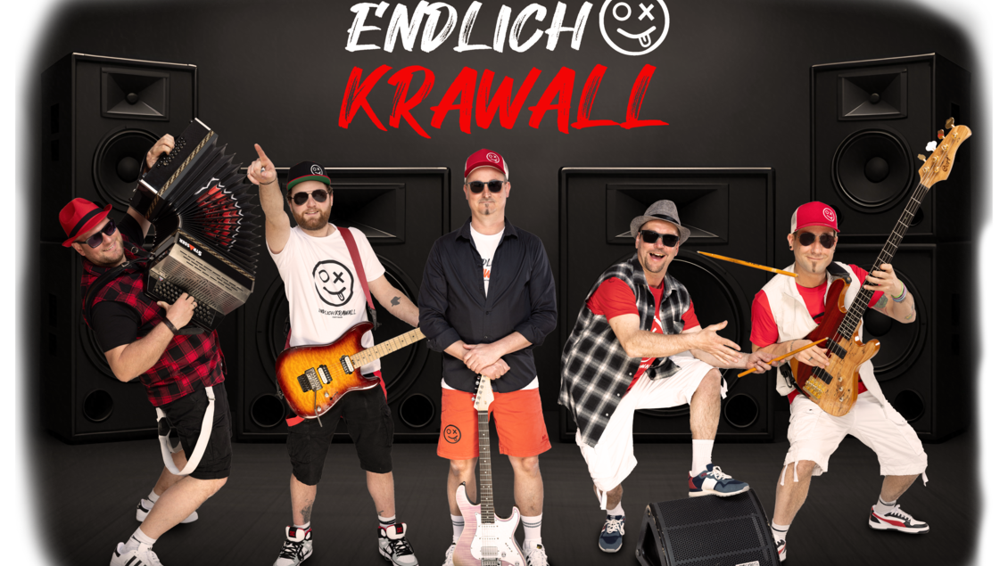 Eine Band steht vor großen Lautsprechern auf einer Bühne. Sie tragen auffällige Outfits und spielen verschiedene Instrumente. | © „ENDLICH-KRAWALL&quot;