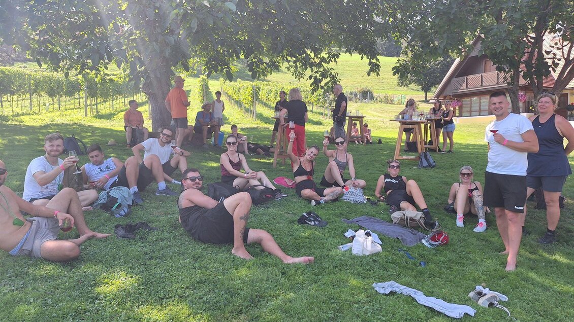 Eine Gruppe von Menschen sitzt entspannt auf dem Rasen unter einem Baum. Im Hintergrund sind Weinreben und ein traditionelles Gebäude zu sehen. | © CDM incoming