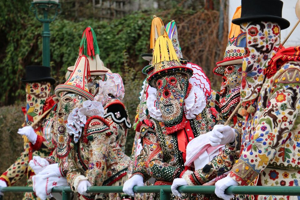 Farbige Gestalten in aufwendigen Kostümen und Masken stehen an einem Geländer. Die festliche Atmosphäre erinnert an einen traditionellen Umzug oder Karneval. | © TVB Ausseerland - Theresa Schwaiger