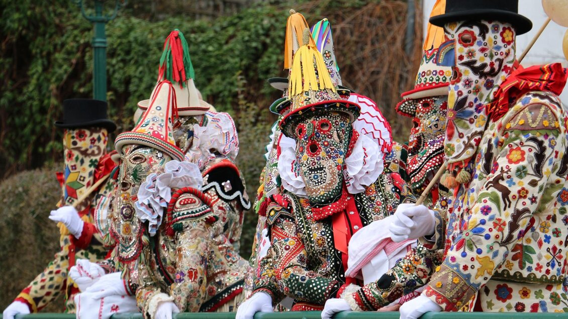 Farbige Gestalten in aufwendigen Kostümen und Masken stehen an einem Geländer. Die festliche Atmosphäre erinnert an einen traditionellen Umzug oder Karneval. | © TVB Ausseerland - Theresa Schwaiger