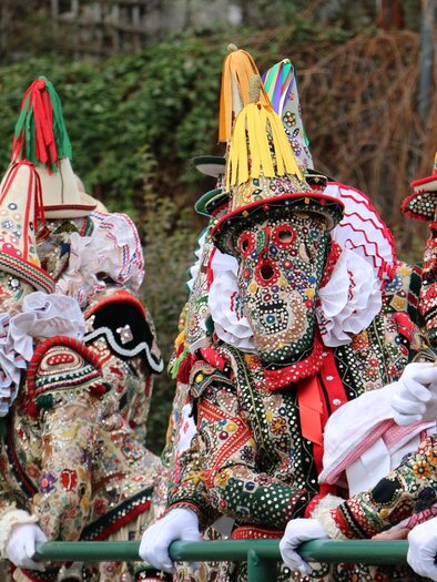 Farbige Gestalten in aufwendigen Kostümen und Masken stehen an einem Geländer. Die festliche Atmosphäre erinnert an einen traditionellen Umzug oder Karneval. | © TVB Ausseerland - Theresa Schwaiger