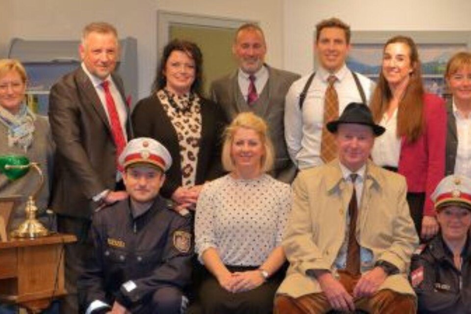 Eine Gruppe von Menschen posiert in einem Innenraum. Einige tragen formelle Kleidung, während andere in Uniformen sind. | © Knoschpnbühne 2024(c) Ausseer Knoschpnbühne