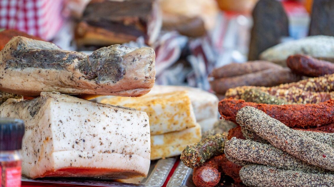 Eine Auswahl an verschiedenen Wurstsorten und Käse auf einem Marktstand. Die Produkte sind liebevoll angerichtet und zeigen unterschiedliche Farben und Texturen. | © Christine Struz