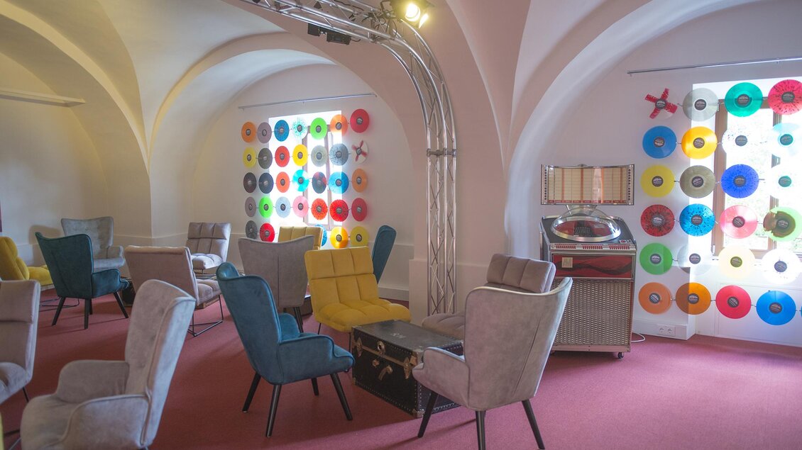 Ein stilvoller Innenraum mit bunten Stühlen und einer Retro-Plattensammlung. Die Wände sind mit farbenfrohen Schallplatten dekoriert und schaffen eine gemütliche Atmosphäre. | © Austro-Pop Zeitreise