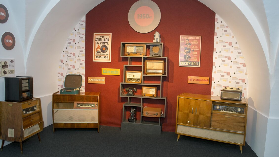 Ein Ausstellungseck mit Vintage-Radios und Plattenspielern. Die Wände sind mit Retro-Postern dekoriert, die eine nostalgische Atmosphäre schaffen. | © Austro-Pop Zeitreise