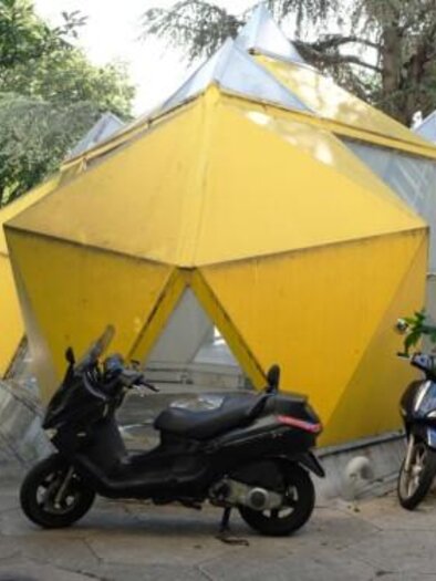 A striking yellow building in geometric shape, surrounded by plants. Next to it are two motorcycles. | © Martin Feiersinger