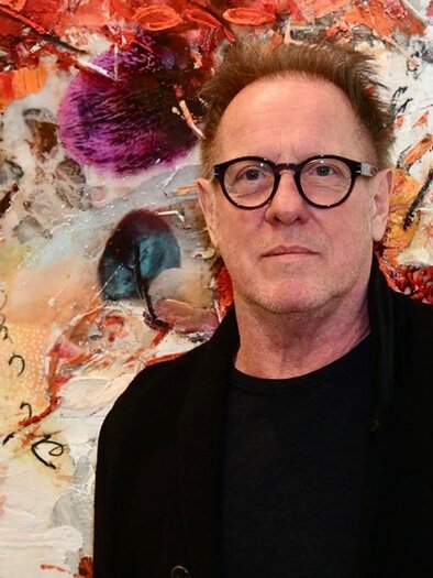 A man with glasses stands in front of a colorful, abstract mural. The colors are vibrant and diverse in an artistic arrangement. | ©  Georg Brandner