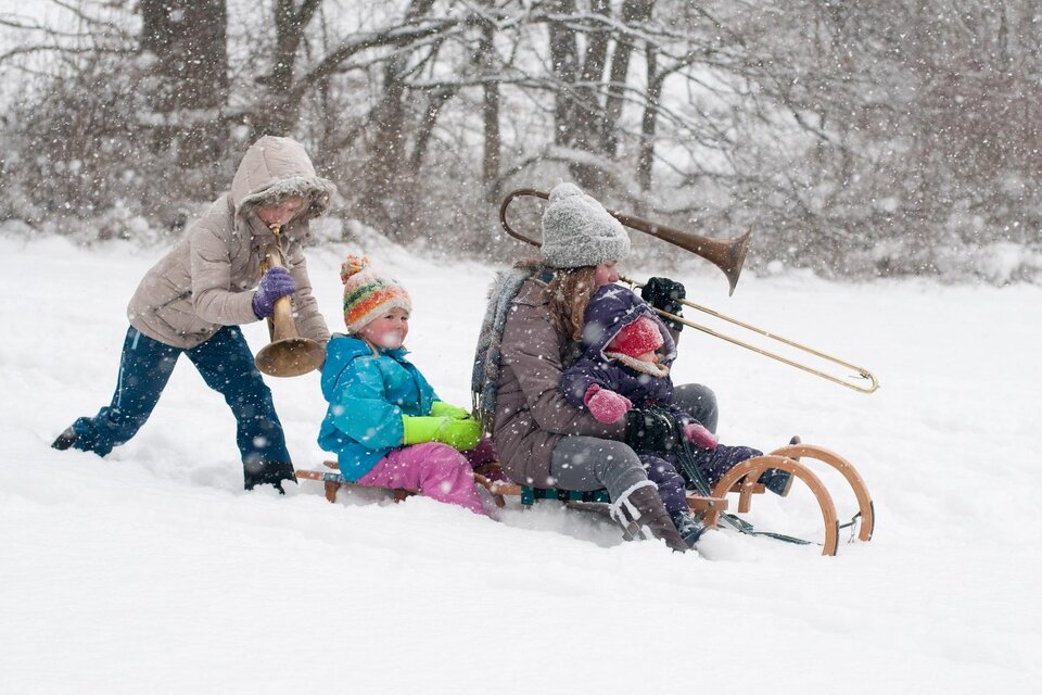 Eine Gruppe von Kindern und Erwachsenen spielt im Schnee. Einige fahren Schlitten, während andere Musikinstrumente spielen. | © (c)STVLW_Unterrainer