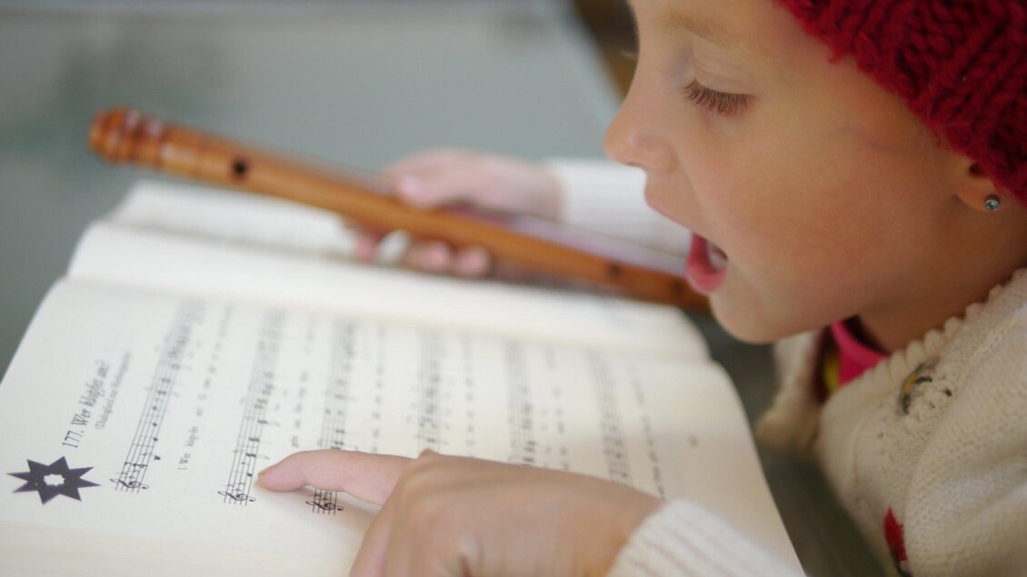 Ein Mädchen spielt Blockflöte und singt dazu. Sie schaut auf ein Notenblatt, während sie musiziert. | © Steirisches Volksliedwerk