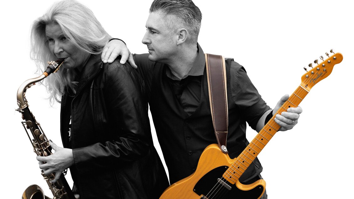 Ein Musikerpaar in Schwarz-Weiß. Die Frau spielt Saxophon, während der Mann eine elektrische Gitarre hält. | © BOSStria