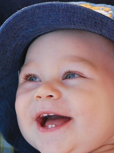 Ein fröhliches Baby mit einem blauen Hut lächelt. Seine Augen strahlen vor Freude.